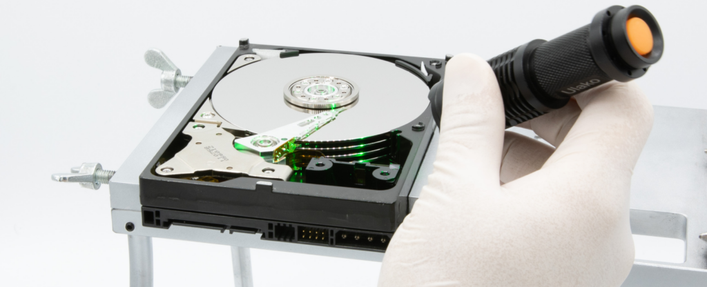Technician examining an open hard drive platter with a flashlight during data recovery.